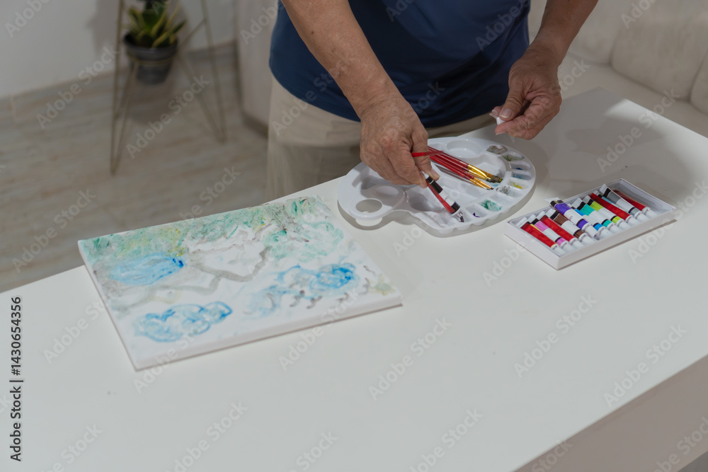 Obraz premium Senior man picking up paintbrushes while painting on canvas at home