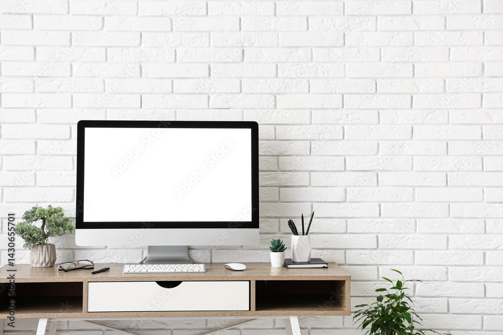 Fototapeta premium Stylish workplace with computer and stationery near white brick wall in light office