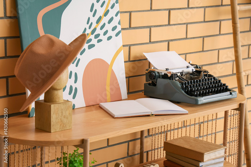 Vintage typewriter, open book and mannequin head with hat on shelving unit near brick wall