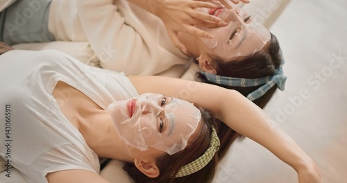 Two Asian women friends applying sheet masks together during beauty daily routine at home. Girl talk, skincare bonding moment, Gen Z lifestyle, self care and relaxing feminine friendship vibe.