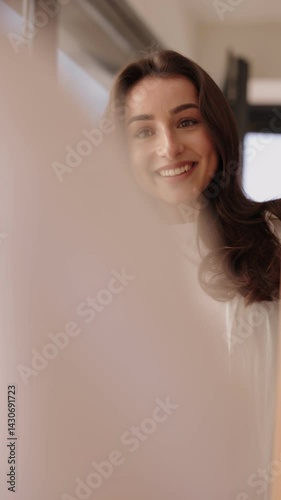 A cheerful woman with dark hair adjusts her hairstyle while looking at her reflection in a mirror, getting ready with confidence.