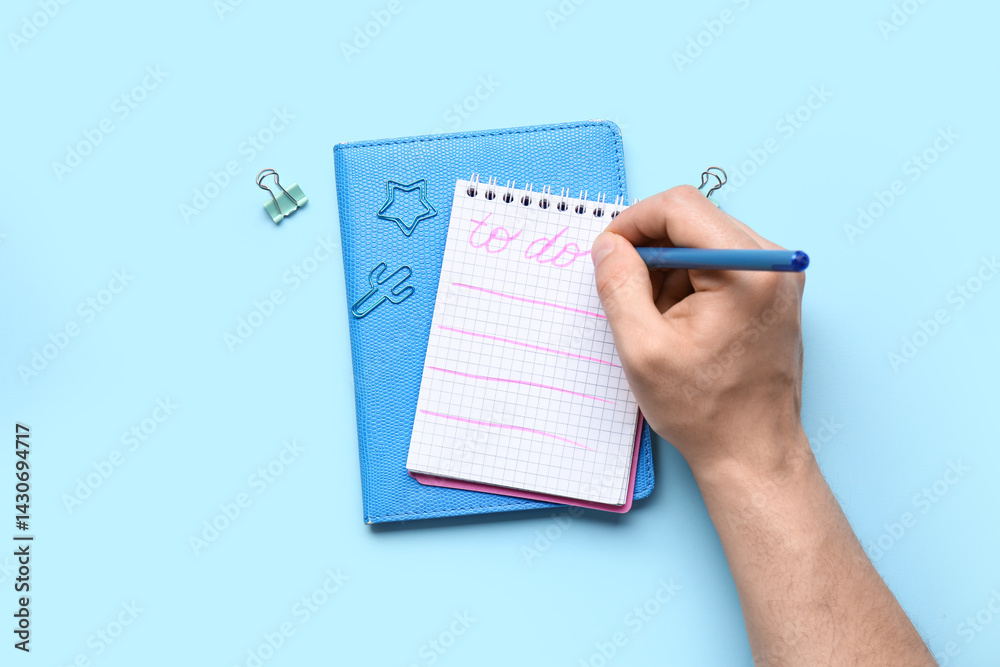 Male hand with to-do list, notebook and stationery on blue background Male hand with to-do list, notebook and stationery on blue background