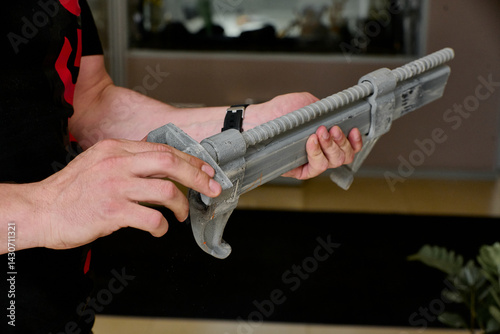 A close-up of a person holding a metal formwork fastener with an integrated threaded rod. The fastener has a ribbed surface 