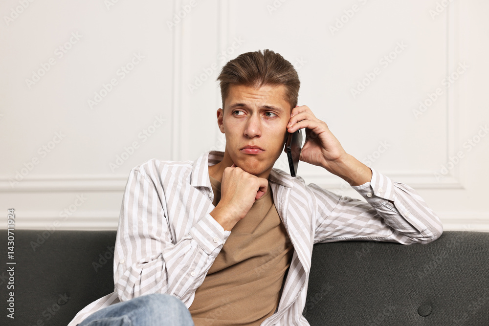 Stressed man calling hotline for mental health help on sofa at home