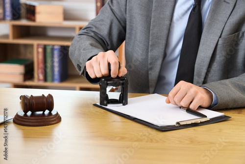 Male lawyer stamping document at table in office, closeup