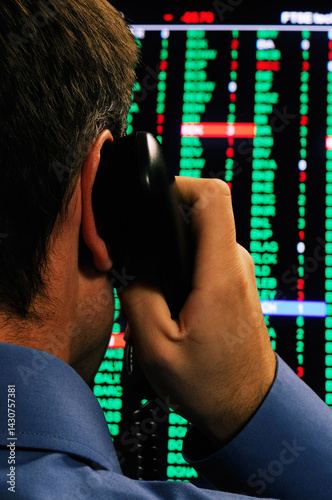 Stockbroker using a phone in front of a display of stock market prices