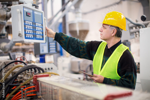 Senior worker in the factory operating machines and taking notes