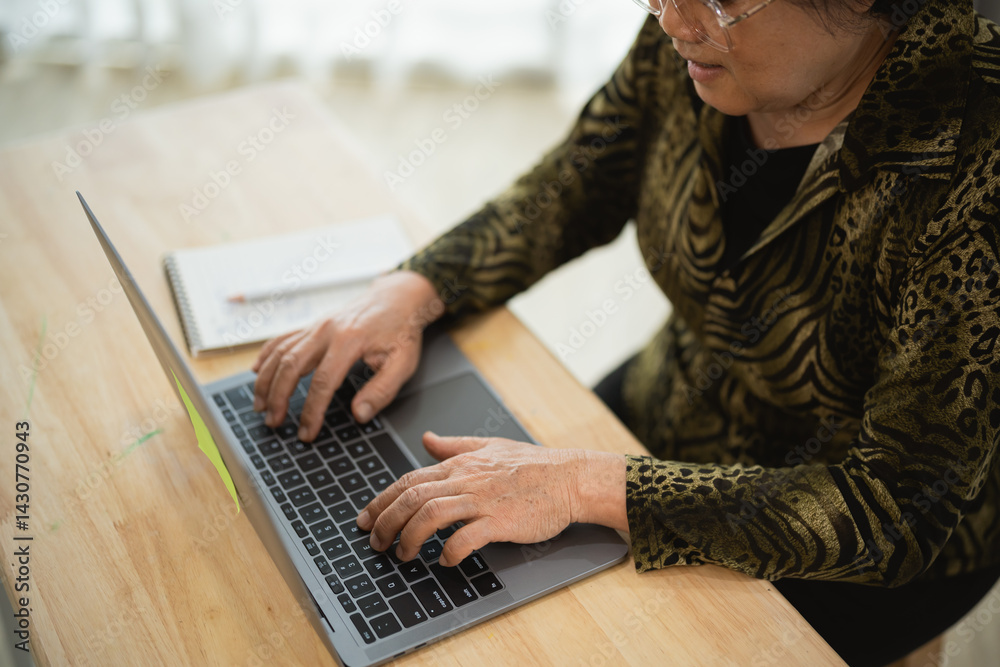 Senior woman working on laptop at home office table with notebook reflecting productivity and modern technology use in everyday life Senior woman working on laptop at home office table with notebook reflecting productivity and modern technology use in everyday life