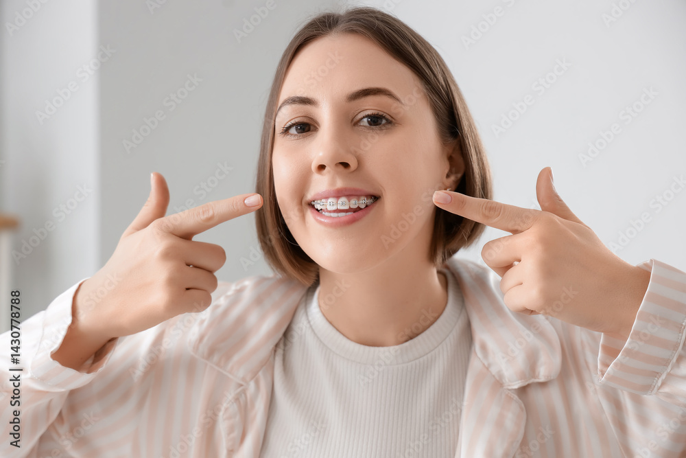 Young woman pointing at her teeth with dental braces in bathroom, closeup