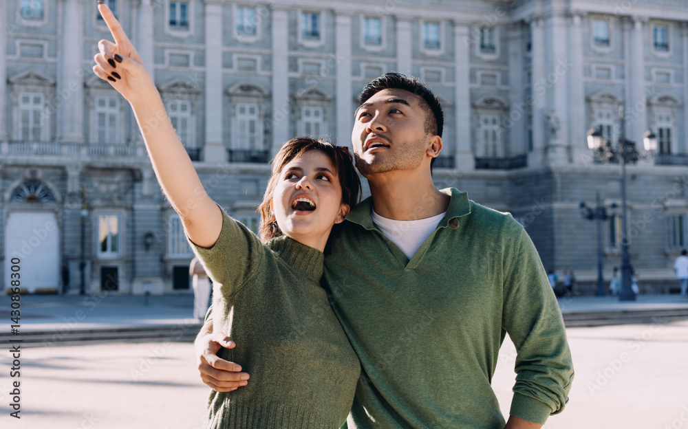 Couple marveling at architecture, woman pointing up in wonder while partner smiles beside her. Romantic moment of shared curiosity during sightseeing in vibrant Madrid