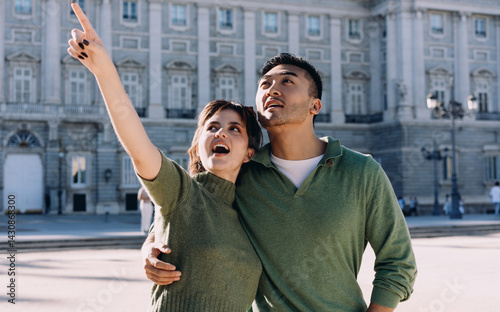 Obraz na płótnie Couple marveling at architecture, woman pointing up in wonder while partner smiles beside her. Romantic moment of shared curiosity during sightseeing in vibrant Madrid w salonie