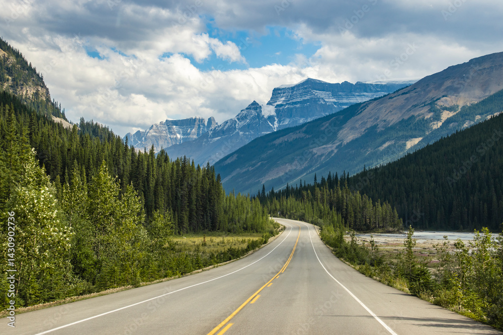 Fototapeta premium Scenic winding road through mountains and forests on a clear day with soft clouds