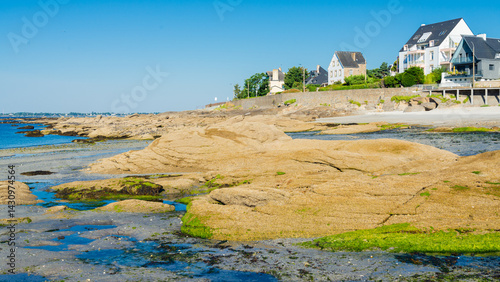 The coastline of Concarneau, Brittany, France, during low tide, with rocks and the waters of Atlantic ocean. Traditional residential houses on the right. Blue sky on the background.