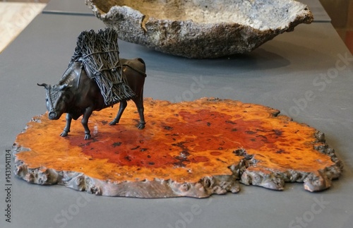 A meticulously crafted bronze ox, laden with a bundle of dried branches, stands on a vibrant slab of wood. photo