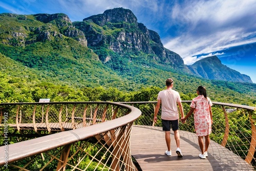 Couple strolls hand in hand along the soaring Boomslang walkway, embracing stunning views of lush foliage and dramatic mountains in Kirstenbosch Botanical Garden, Cape Town, South Africa.