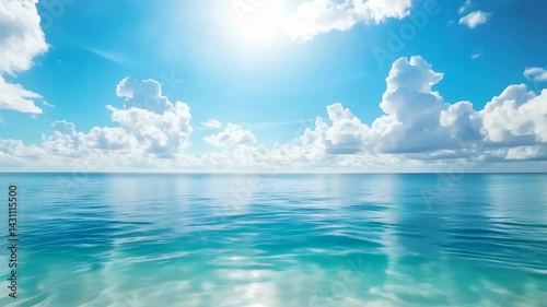 A tranquil ocean view under a bright blue sky, featuring gently rippling water and fluffy clouds reflecting sunlight.