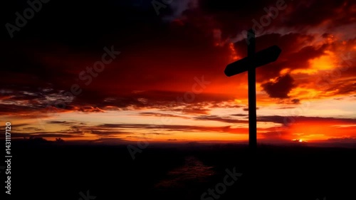 A wooden cross stands alone in a misty field against a vibrant, sunset sky, creating a poignant and serene atmosphere.