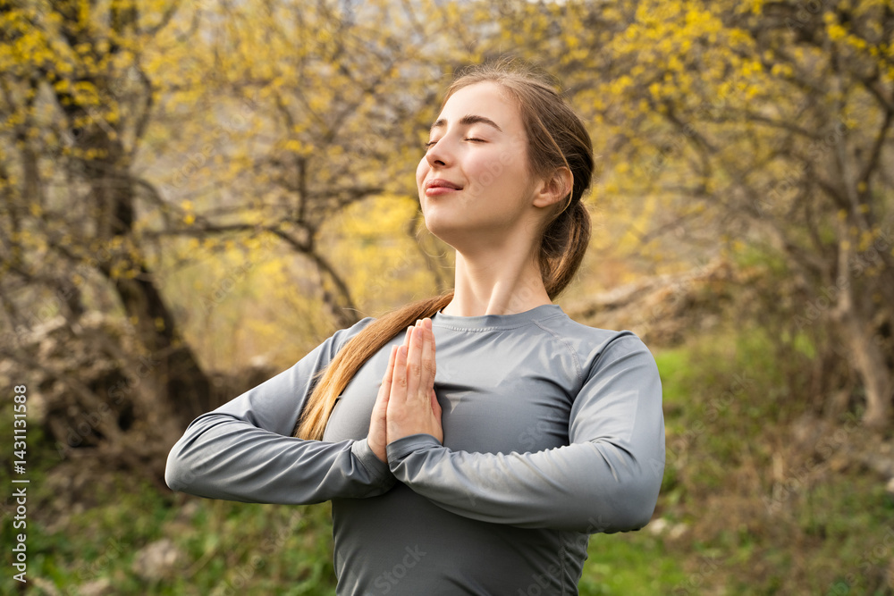 Peaceful young woman meditating in sunlight in nature park, holding hands in namaste, practicing yoga meditation, doing breathing exercise outdoors. Wellness, wellbeing, gratitude zen, energy balance Peaceful young woman meditating in sunlight in nature park, holding hands in namaste, practicing yoga meditation, doing breathing exercise outdoors. Wellness, wellbeing, gratitude zen, energy balance