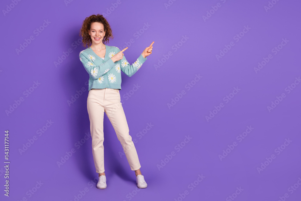 Smiling young woman pointing to the side on a purple background wearing a floral cardigan Casual and whimsical fashion concept Smiling young woman pointing to the side on a purple background wearing a floral cardigan Casual and whimsical fashion concept