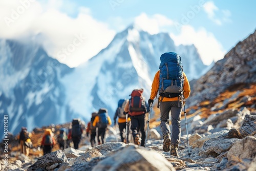 Obraz na płótnie A group of mountaineers hikes along a rocky trail in the high mountains, wearing warm gear and large backpacks, surrounded by snowy peaks. w salonie