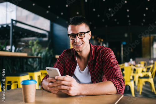 Smiling man in glasses using mobile phone in cafeteria
