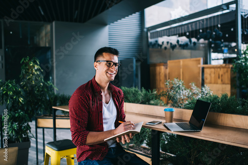 Cheerful young man sitting with laptop in cafe