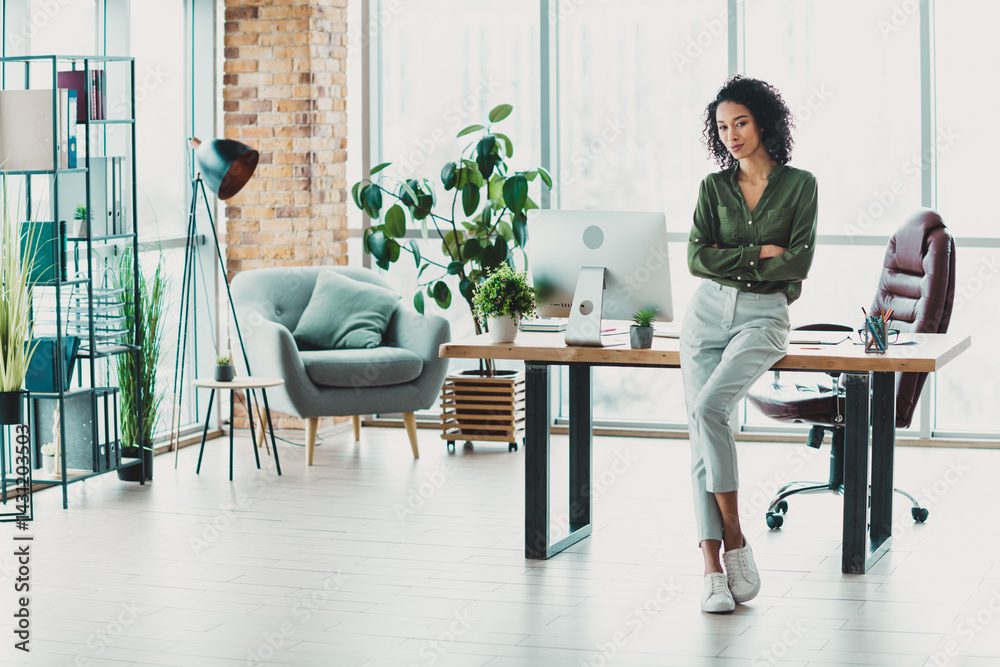 Young businesswoman standing confidently in modern daylight office with stylish casual attire and a green shirt, showcasing professionalism Young businesswoman standing confidently in modern daylight office with stylish casual attire and a green shirt, showcasing professionalism