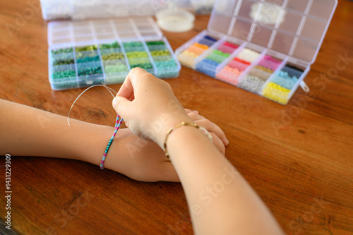 Child making beaded bracelets at home using colorful glass seed beads. Focused creative activity, fine motor skills development, peaceful indoor moment.