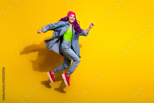 Wallpaper Mural Stylish young woman jumping with joy on a vibrant yellow background wearing denim, a pink beanie, and trendy colorful attire Torontodigital.ca