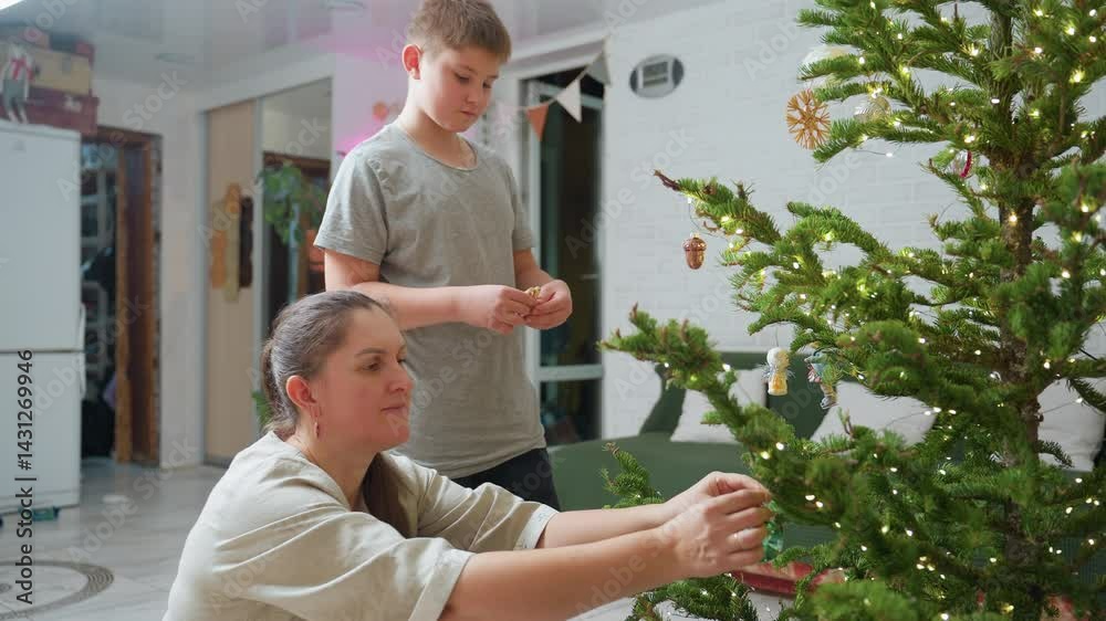 Mother handing ornament to son while fixing another ornament on christmas tree, joyful festive indoor scene, preparing holiday decorations together in warm cozy atmosphere with glowing lights