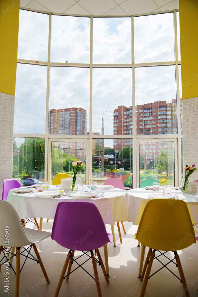 round tables served with dishes and white tablecloths with multi-colored chairs