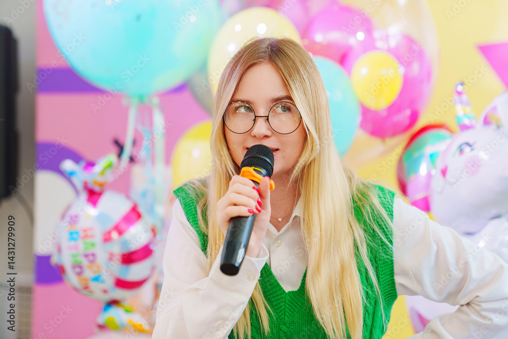 A funny young woman with a microphone is leading a children's party.