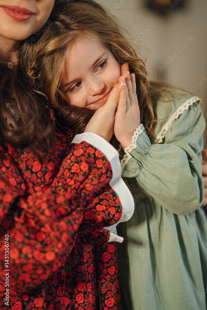 Mom gently hugs her little beautiful daughter in a green dress.