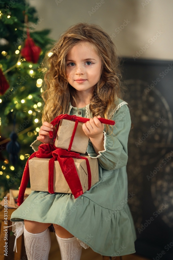 Beautiful little girl with gift boxes at the Christmas tree.