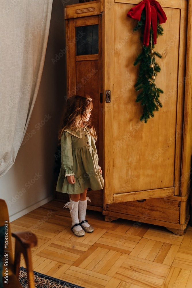 A beautiful cute girl is sitting in a closet by the Christmas tree.