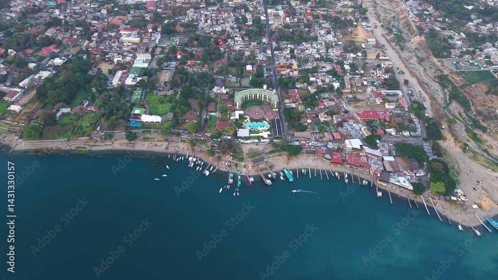 Beautiful cinematic aerial view os the Panajachel town surrounded by Toliman and Atitlan volcanoes, next to the Atitlan lake its piers and traditional fisher and tourist boats - Guatemala