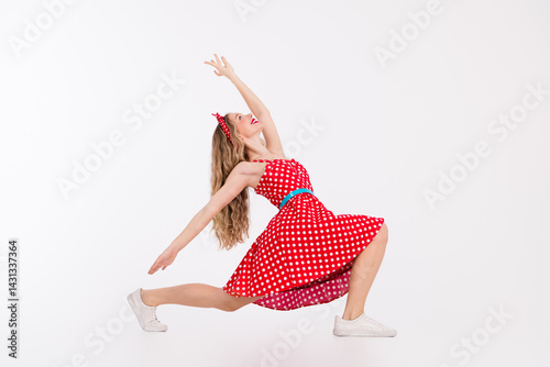 Photography Energetic young woman posing in a retro polka dot dress exudes joy and fun with her cheerful dance move against a white background