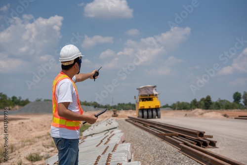 Obraz na płótnie Construction Supervisor Directing Operations: An industrious construction supervisor, equipped with essential safety gear, expertly directs the team at the construction site amidst a bright blue sky. w salonie