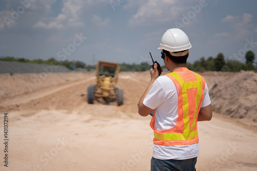 Obraz na płótnie Construction Site Supervisor: A construction site supervisor, equipped with safety attire and a walkie-talkie, surveys a road construction project, embodying vigilance and efficiency. w salonie