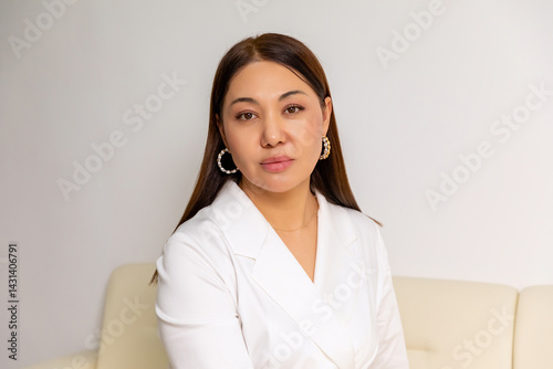 Obraz na płótnie Head shot portrait smiling Asian young woman doctor looking at camera, sitting on couch. Attractive female blogger shooting vlog for social network, teacher coach recording webinar, working at home w salonie