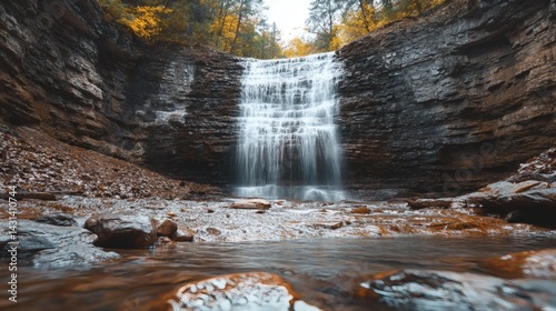 Autumn waterfall cascading down rocky cliffs, forest background; nature photography