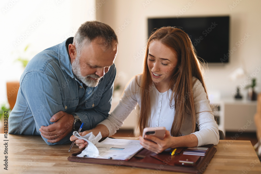 Couple discussing financial documents while using mobile phone in cozy home office setting Couple discussing financial documents while using mobile phone in cozy home office setting