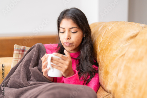 Relaxing indoors with a warm drink while wrapped in a cozy blanket during a chilly evening at home