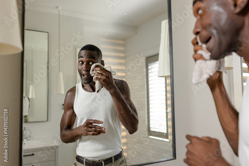 African American man dabbing face with washcloth before mirror in bathroom, with pendant light