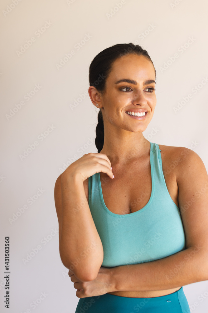 Smiling woman crossing arms and looking right in studio, wearing turquoise sports bra and leggings Smiling woman crossing arms and looking right in studio, wearing turquoise sports bra and leggings