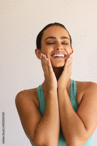 Wallpaper Mural Smiling woman in early 20s pressing cheeks against off-white wall, wearing teal sports bra Torontodigital.ca