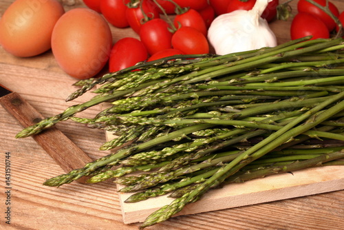 Bunch of wild asparagus arranged on a wooden cutting board with other dinner ingredients.