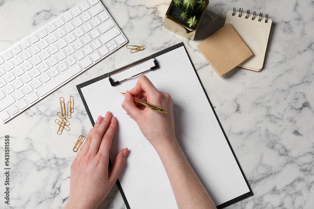 Woman writing in clipboard at white marble table, top view