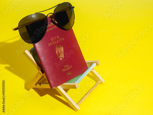 Passport of Ireland with dark sunglasses in sun bed on yellow sand like surface and blue ocean background. Irish love for exotic and sunny holiday concept. Immigration to sunny places theme.
