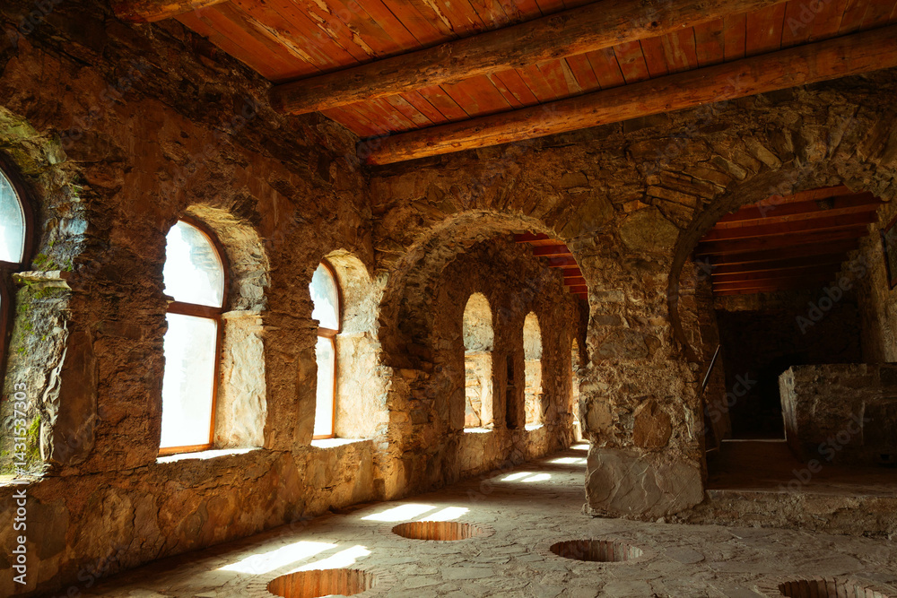Fototapeta premium Traditional Georgian wine cellar with sunlit arched windows and underground clay vessels (qvevri) embedded in the stone floor. Historic winemaking architecture in the Kakheti region